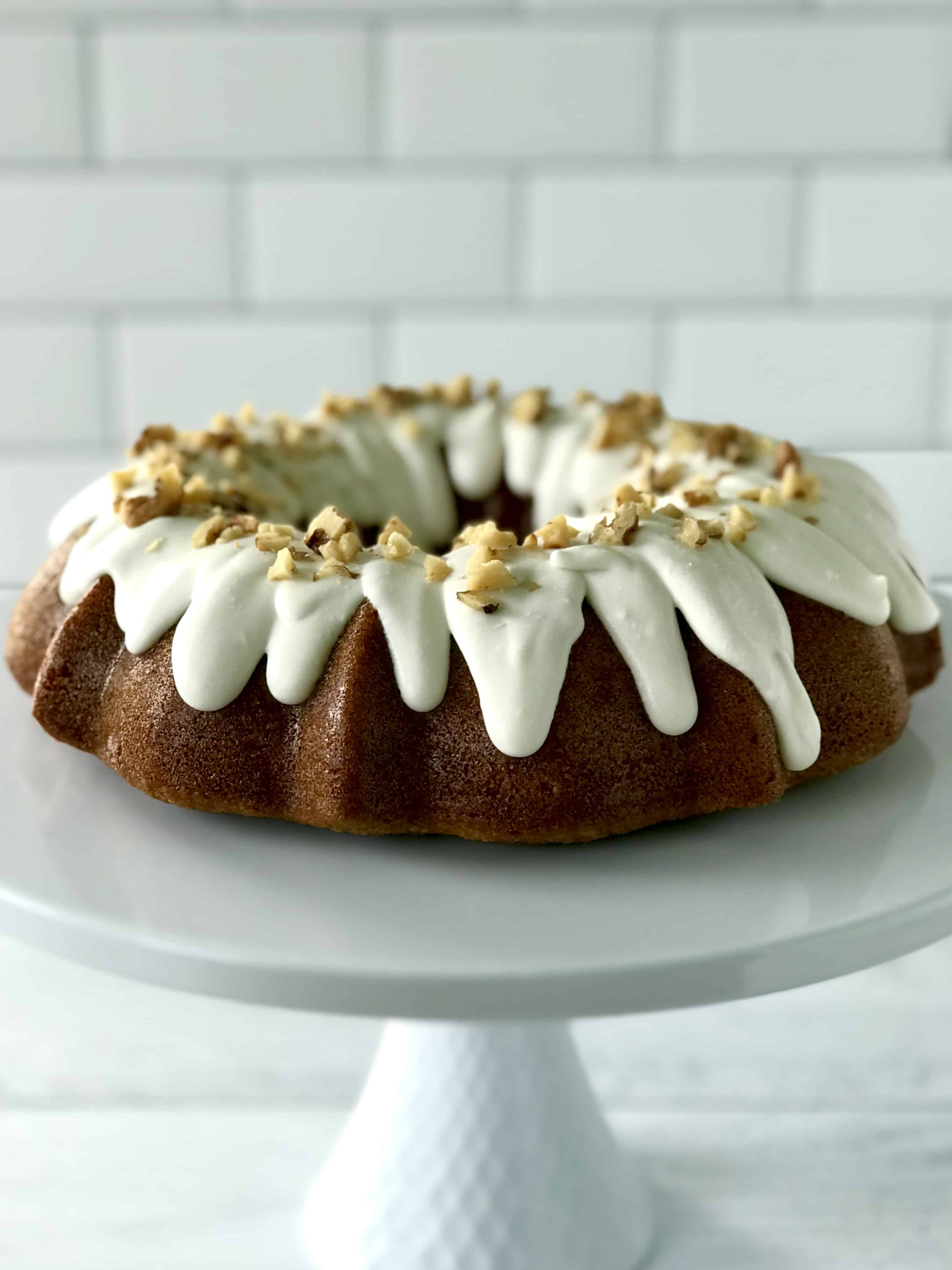 a grain-free cake with a white icing and topped with chopped nuts sitting on a white cake stand