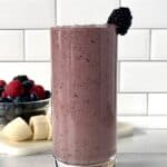 a berry smoothie in a tall glass topped with a blackberry