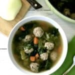 A paleo meatball and vegetable soup in a white bowl next to a green napkin with a spoon on it