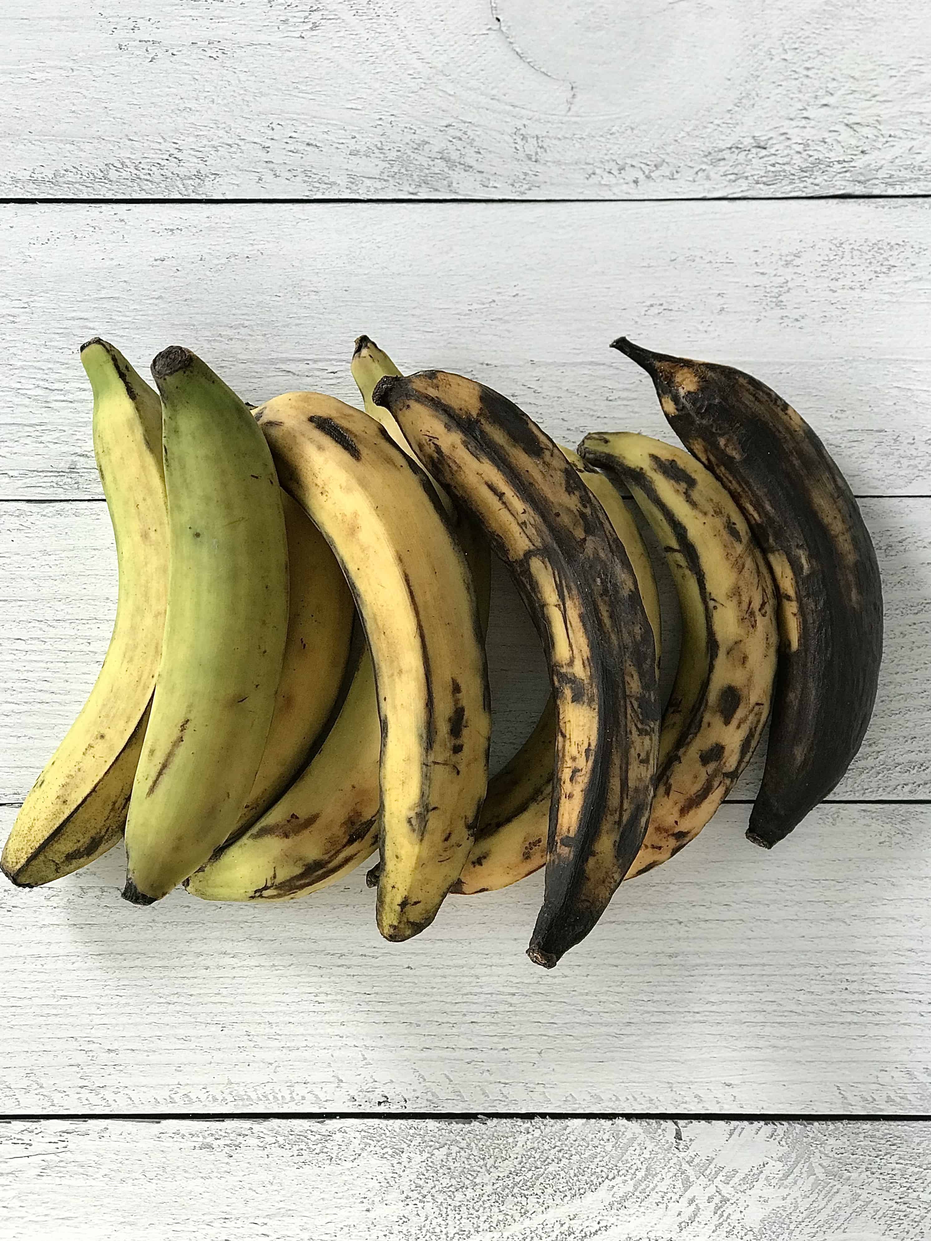 plantains in different stages of ripeness lined up on a white wooden table