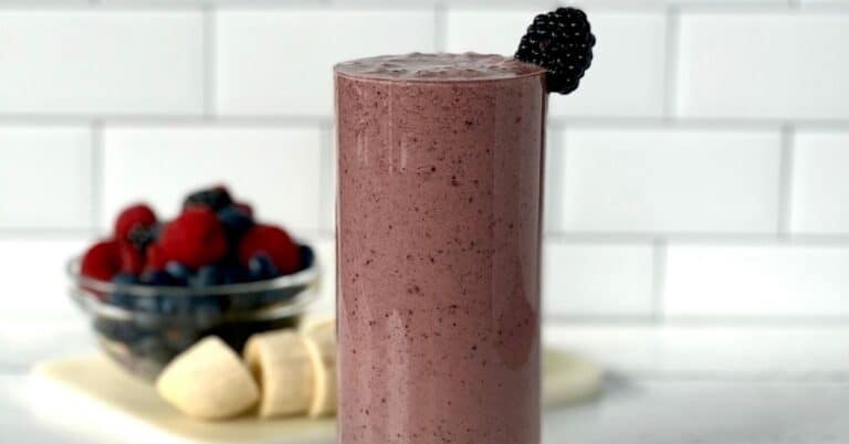 a healthy smoothie made with berries and bananas in a tall glass garnished with a blackberry