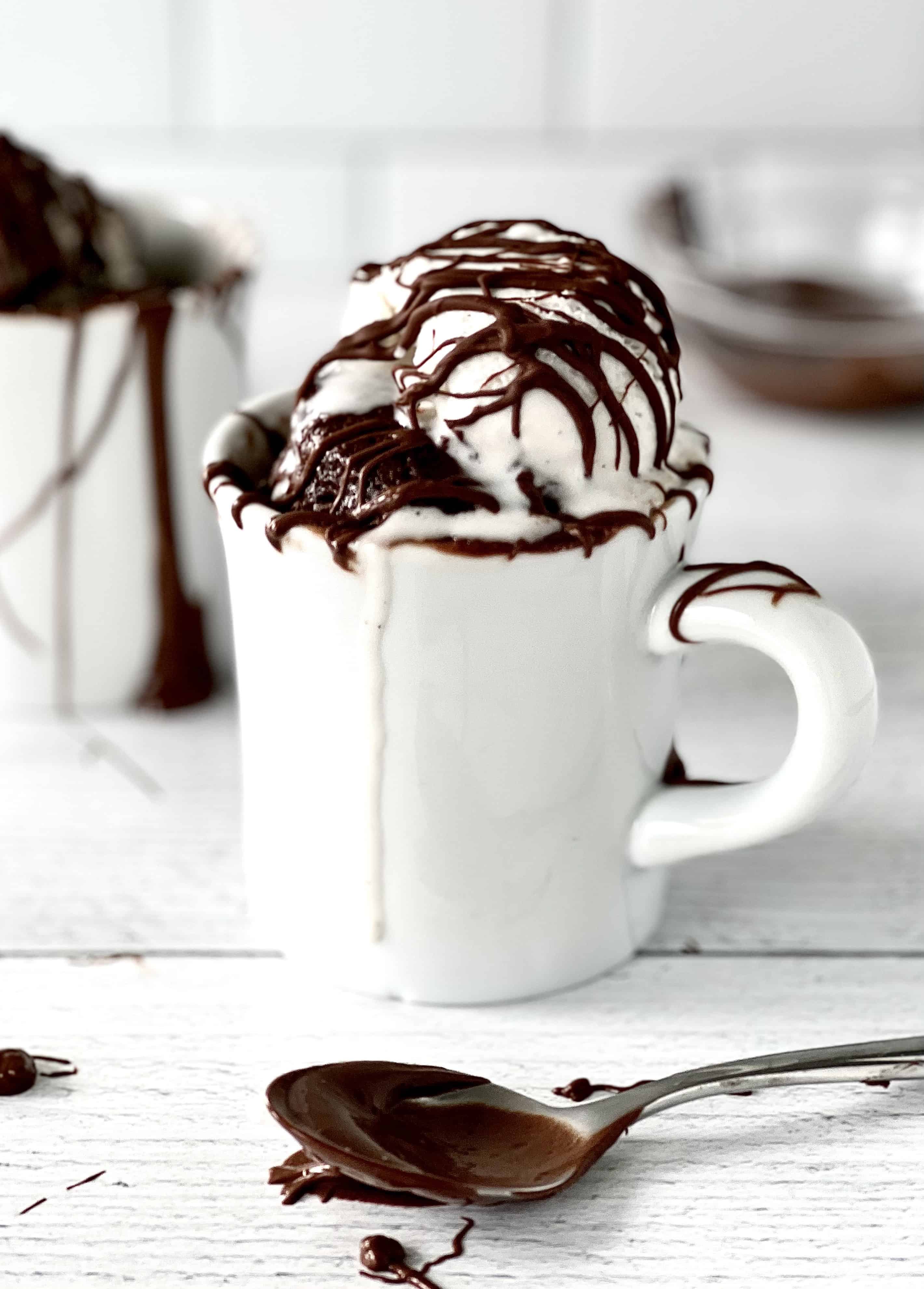 a gluten-free chocolate hazelnut cake in a white mug topped with vanilla ice cream and more chocolate hazelnut sauce drizzled on top