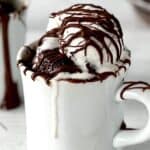 a chocolate hazelnut grain-free mug cake in a white mug topped with vanilla ice cream and drizzles of chocolate hazelnut sauce