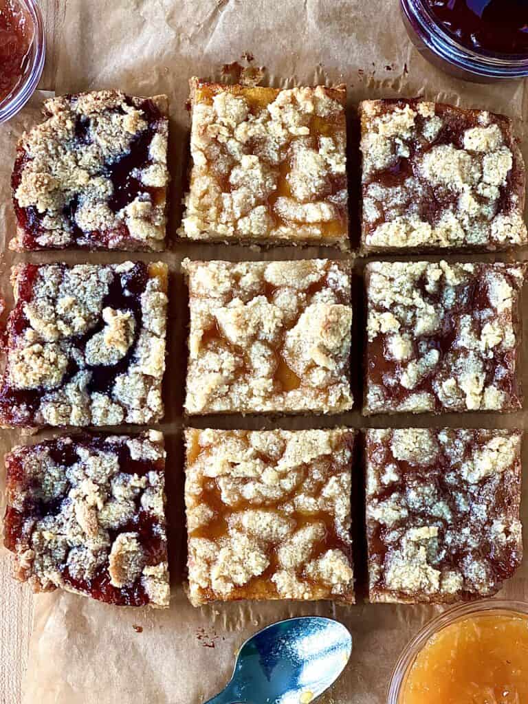 3 different flavors of vegan crumble bars on parchment paper next to bowls of jams and a spoon