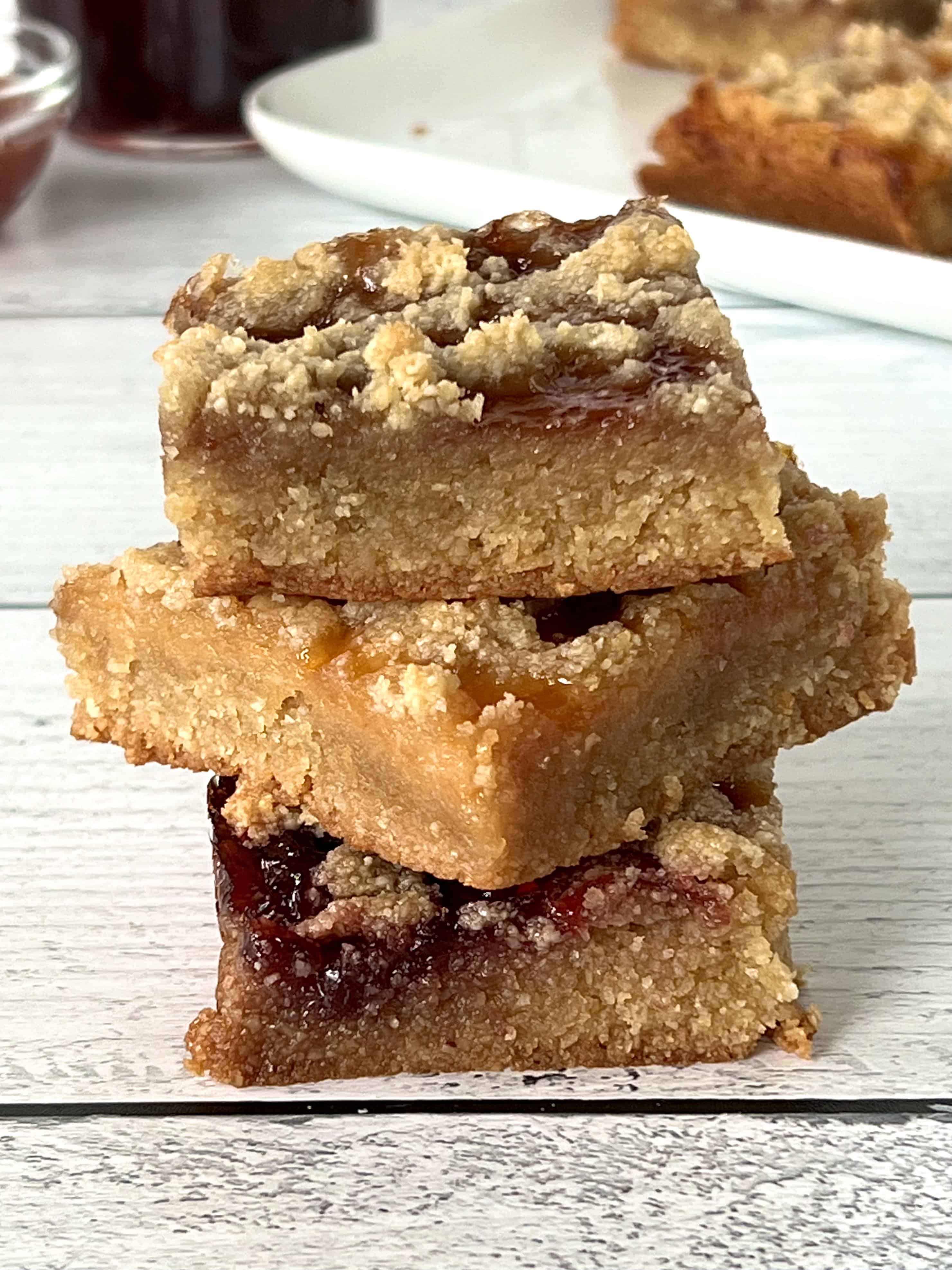 3 different flavors of gluten-free crumb bars stacked on top of each other on a white wooden table