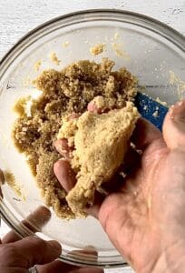a clump of shortbread dough held by a hand over a glass bowl with more of the dough