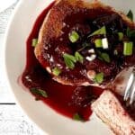 a pork chop on a white plate covered in a chunky cherry sauce