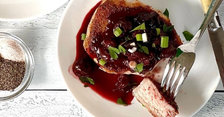 a pork chop on a white plate covered in a chunky cherry sauce