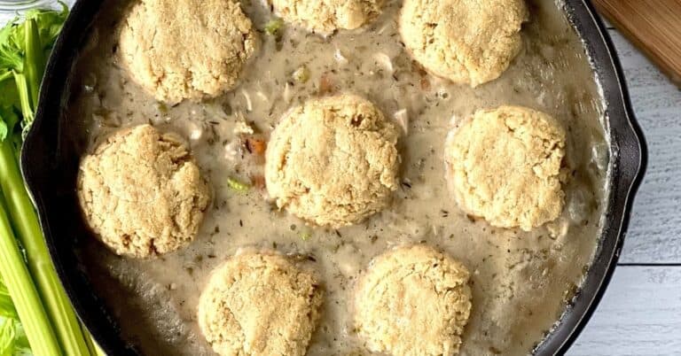 almond flour biscuits on top of chicken pot pie filling in a large cast iron skillet next to celery