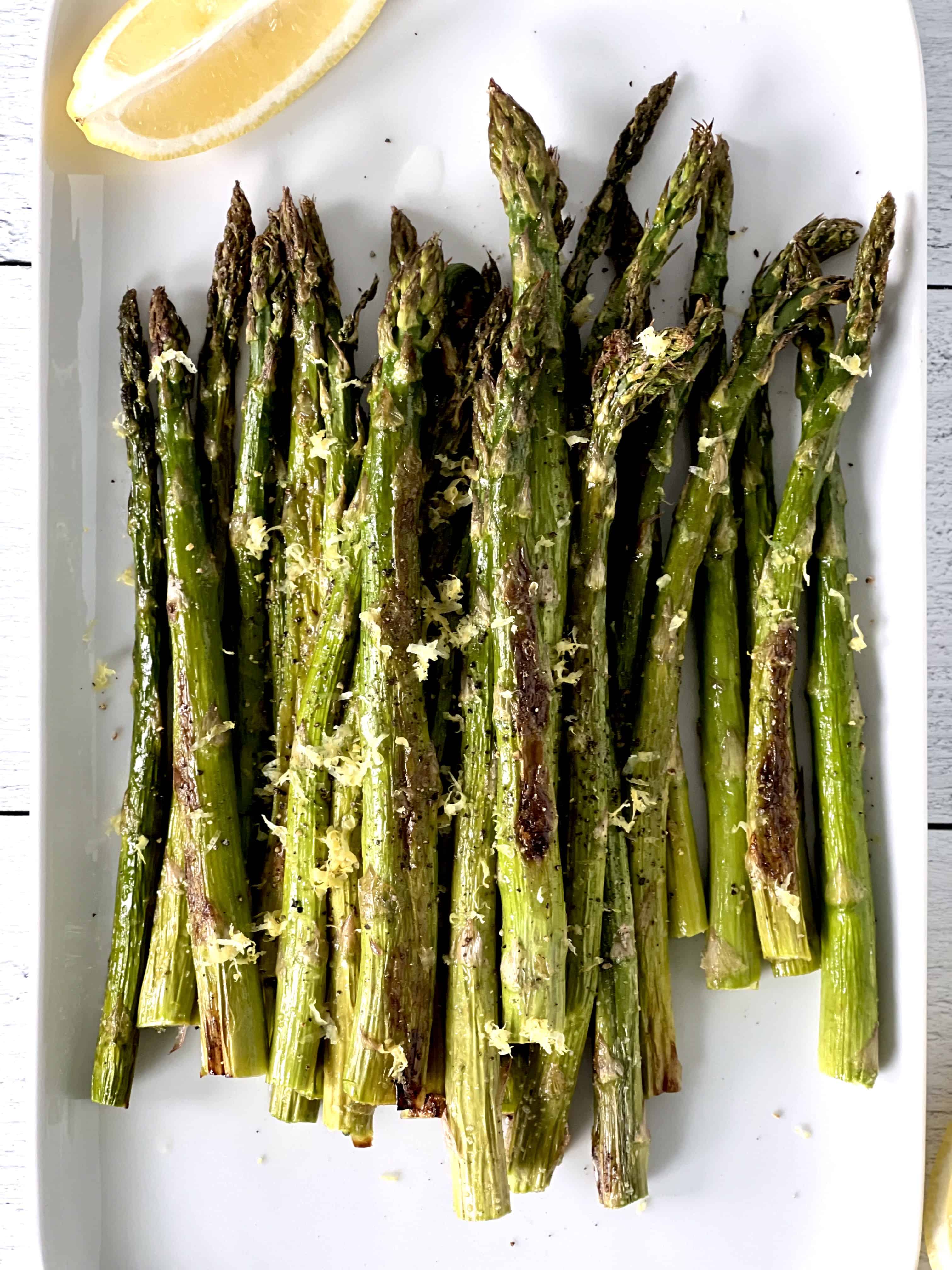 a rectangular white platter with roasted asparagus and a lemon wedge on it