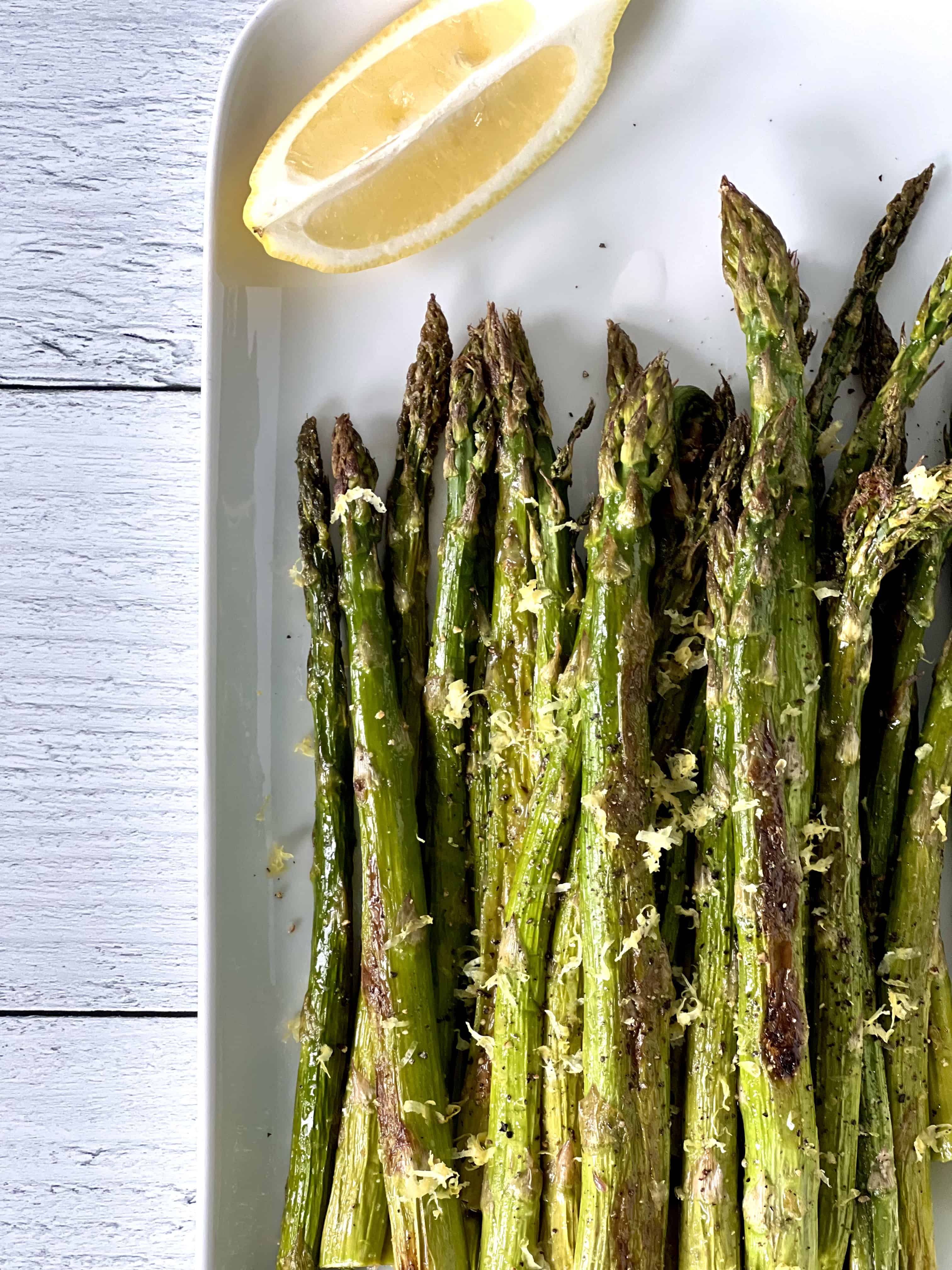 asparagus baked in the oven on a white platter with a lemon wedge