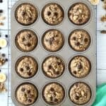 grain-free banana muffins with chocolate chips and walnuts in muffin cups in a muffin pan on a cooling rack on a white wooden table