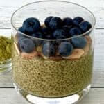 chia pudding made with green tea powder in a glass, topped with blueberries and sliced almonds, next to a small bowl of the green tea powder