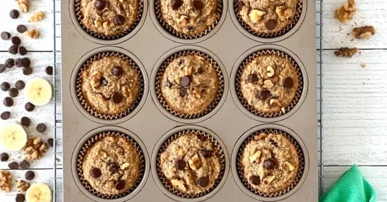 gluten-free banana muffins with chocolate chips and walnuts in a muffin pan on a cooling rack on a white wooden table