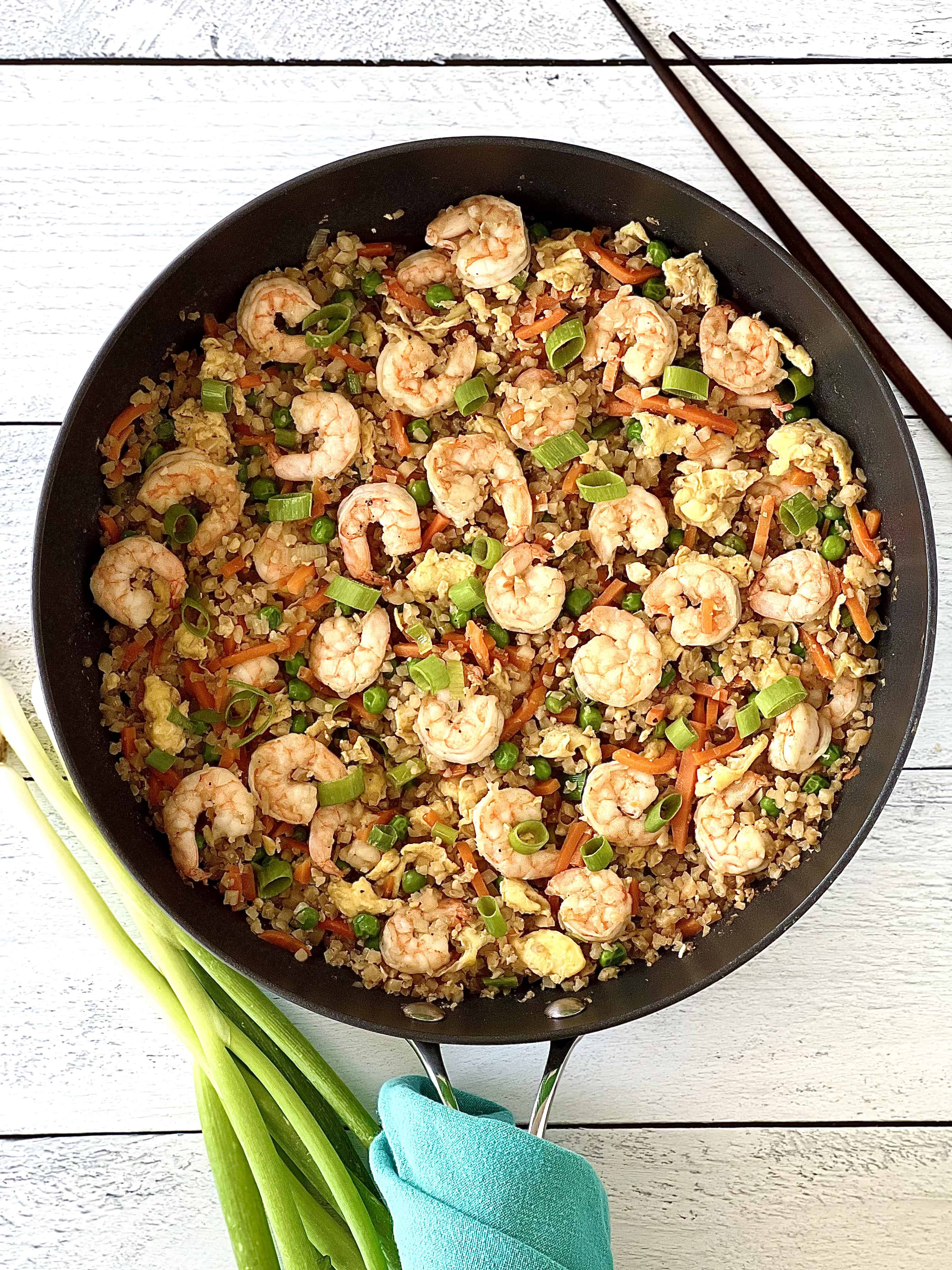 gluten-free Chinese shrimp and cauliflower rice in a large skillet next to chopsticks and scallions on a white wooden table