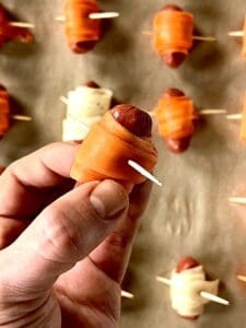a hand holding a little smokie sausage wrapped in a carrot strip and secured with a toothpick