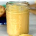 healthy honey lemon curd in a mason jar in front of a blue swirl plate with two English muffin halves spread with the curd