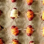 cocktail sausages wrapped in strips of carrots, parsnips or sweet potatoes, with toothpicks through them, lined up on a parchment-lined baking sheet