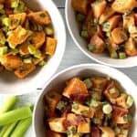 Whole30 sweet potato salad in 3 white bowls on a white wooden table with celery stalks on it