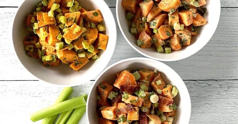 Whole30 sweet potato salad in 3 white bowls on a white wooden table with celery stalks on it