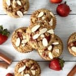 grain-free muffins with strawberries and rhubarb, plus sliced almonds on top, on a white wooden table with rhubarb stalks and strawberries