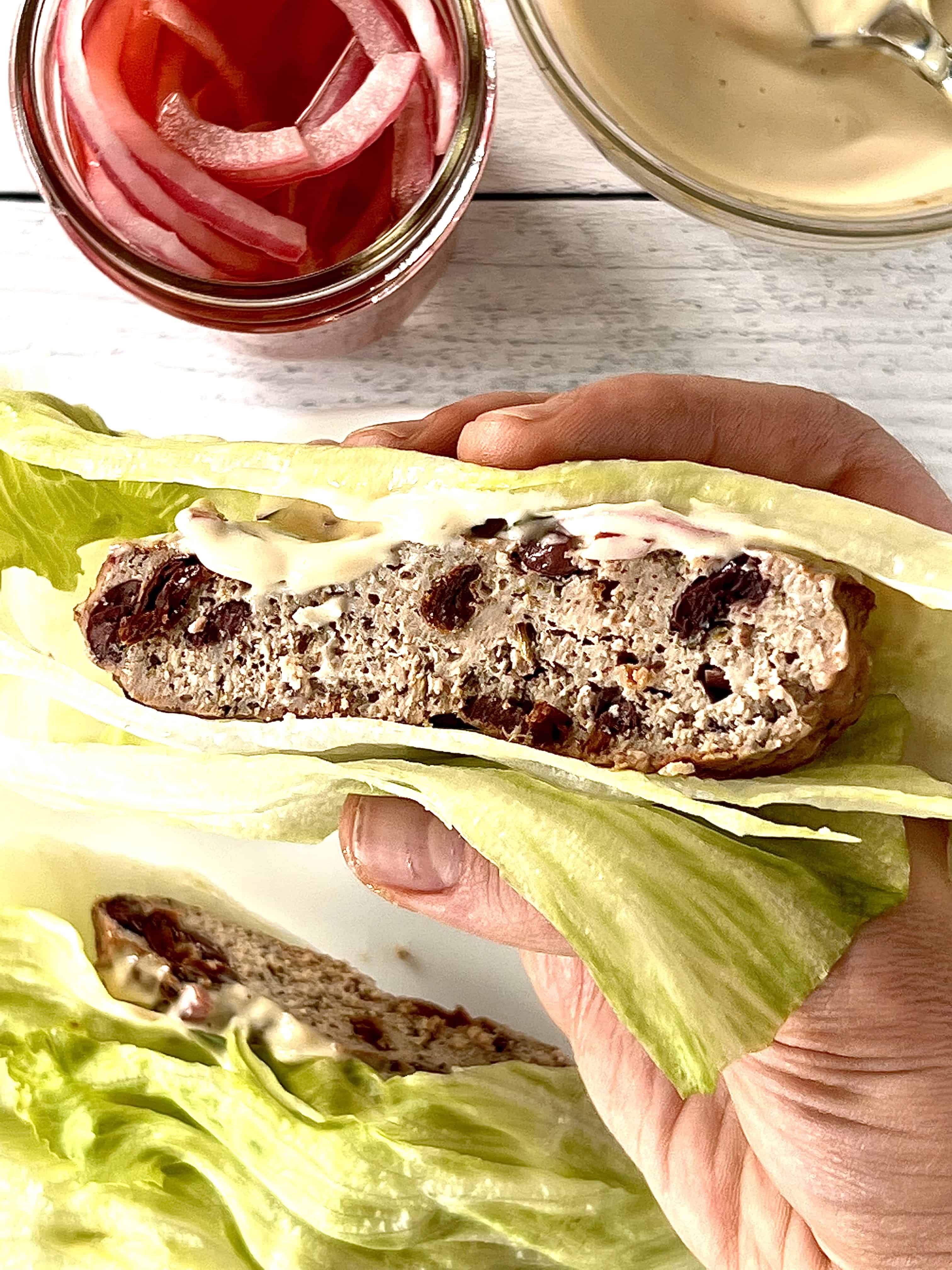 a hand holding up a keto turkey burger on lettuce cups cut in half