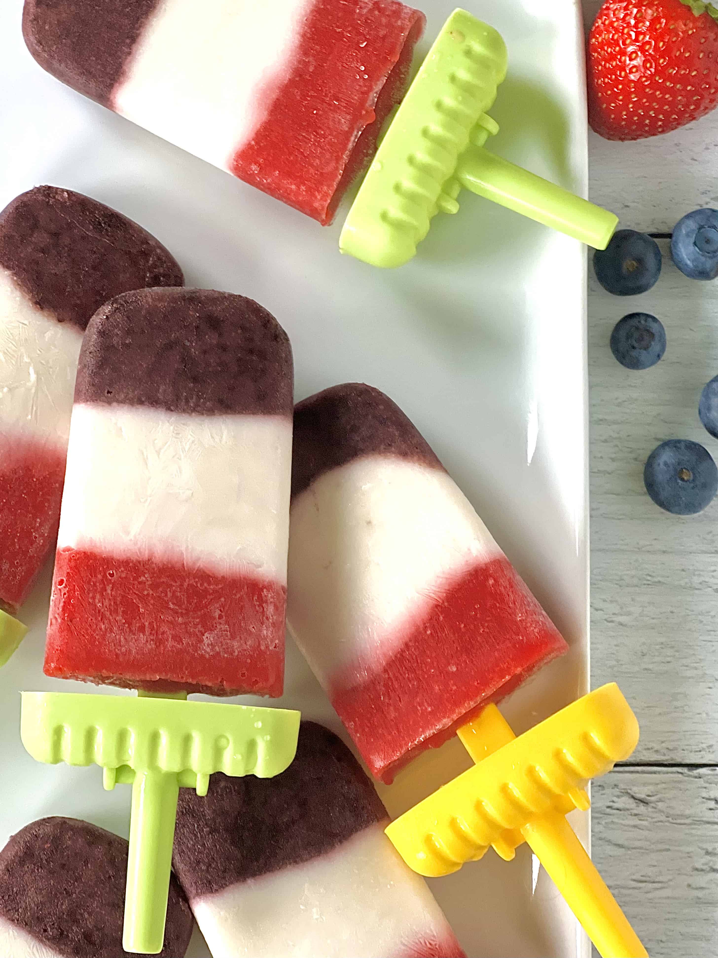 homemade paleo popsicles with layers of real fruit like blueberries and strawberries on a white platter