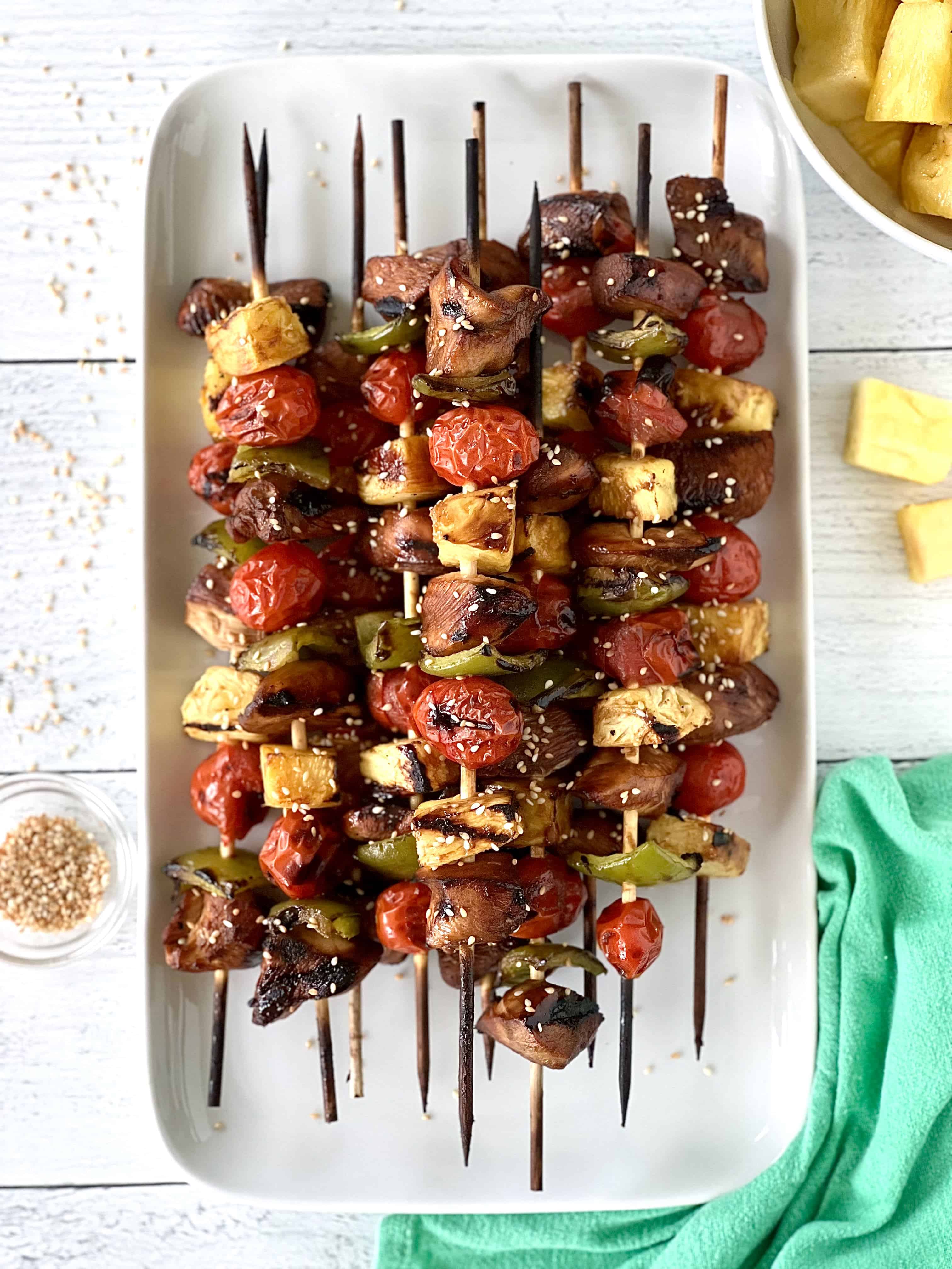 grilled chicken skewers with peppers, cherry tomatoes and pineapple on a long white platter