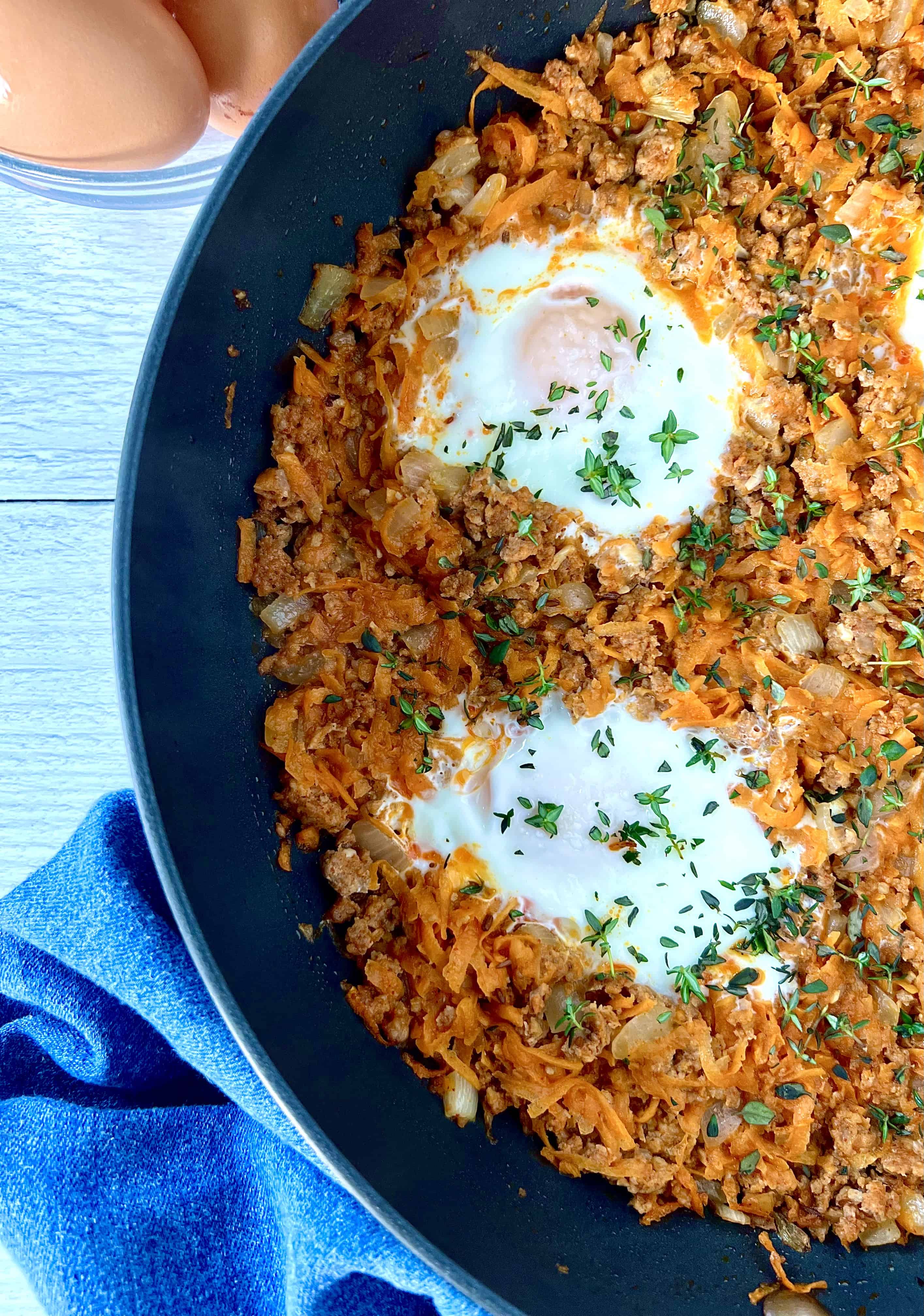 a health hash made with sweet potatoes, chorizo sausage and eggs in a large skillet next to a blue towel