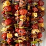 Whole30 chicken skewers with peppers, cherry tomatoes and pineapple on a white platter next to 2 pineapple chunks and a small bowl of sesame seeds