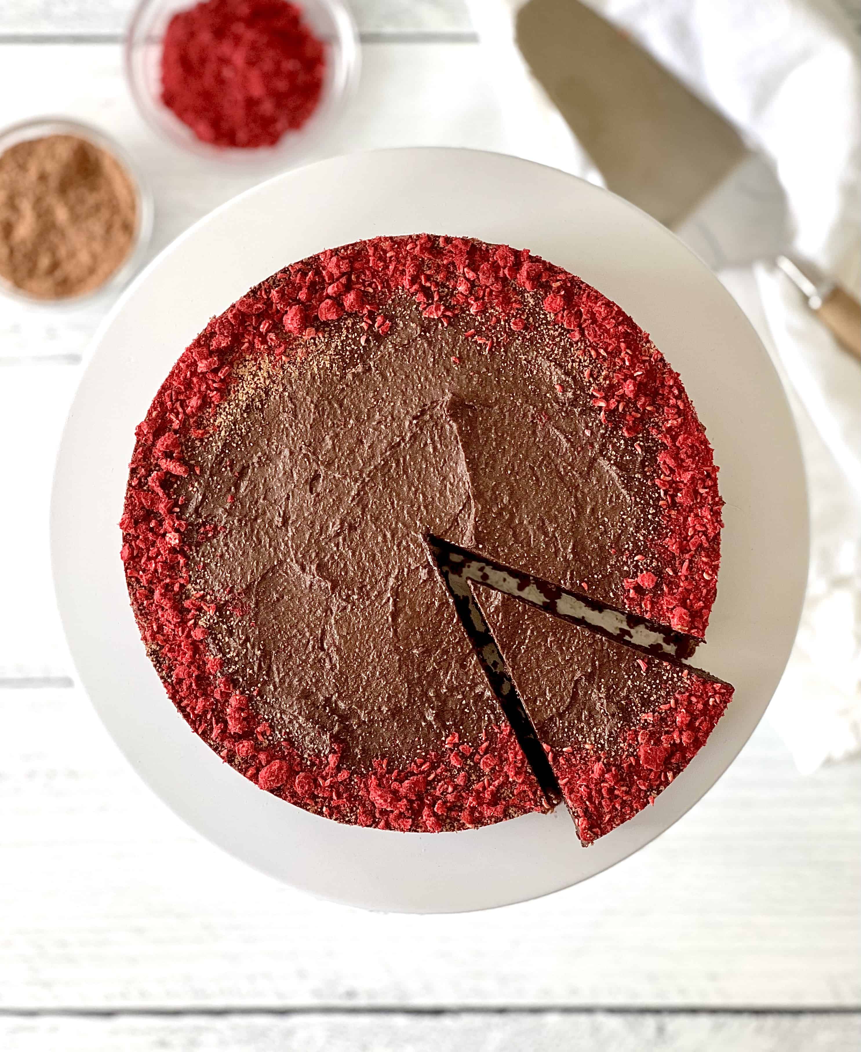 a dairy-free chocolate tart with the edge dusted with crushed freeze-dried raspberries, sitting on a white cake stand