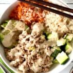 grain-free sushi bowl with canned tuna, vegetables, avocado and a creamy sauce with chopsticks on the rim of the bowl and a fork on a green napkin next to the white bowl