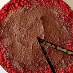 a flourless chocolate tart with the edge dusted with crushed freeze-dried raspberries, sitting on a white cake stand