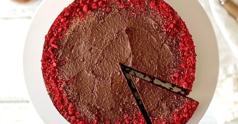 a flourless chocolate tart with the edge dusted with crushed freeze-dried raspberries, sitting on a white cake stand