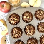 gluten-free apple muffins made with almond flour sitting in a metal muffin pan on a cooling rack surrounded by apple slices, an apple and a jar of applesauce