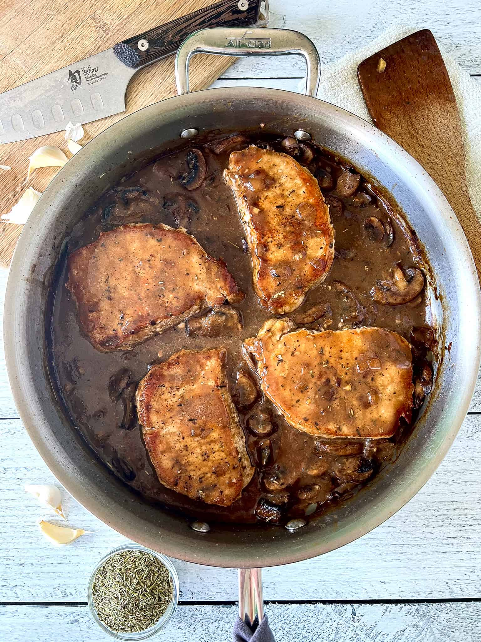 healthy pork chops and a mushroom sauce with no cream in a stainless steel saute pan on a white wooden table