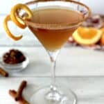 A chai vodka martini in a martini glass with a cinnamon sugar rim and an orange peel twist on the rim