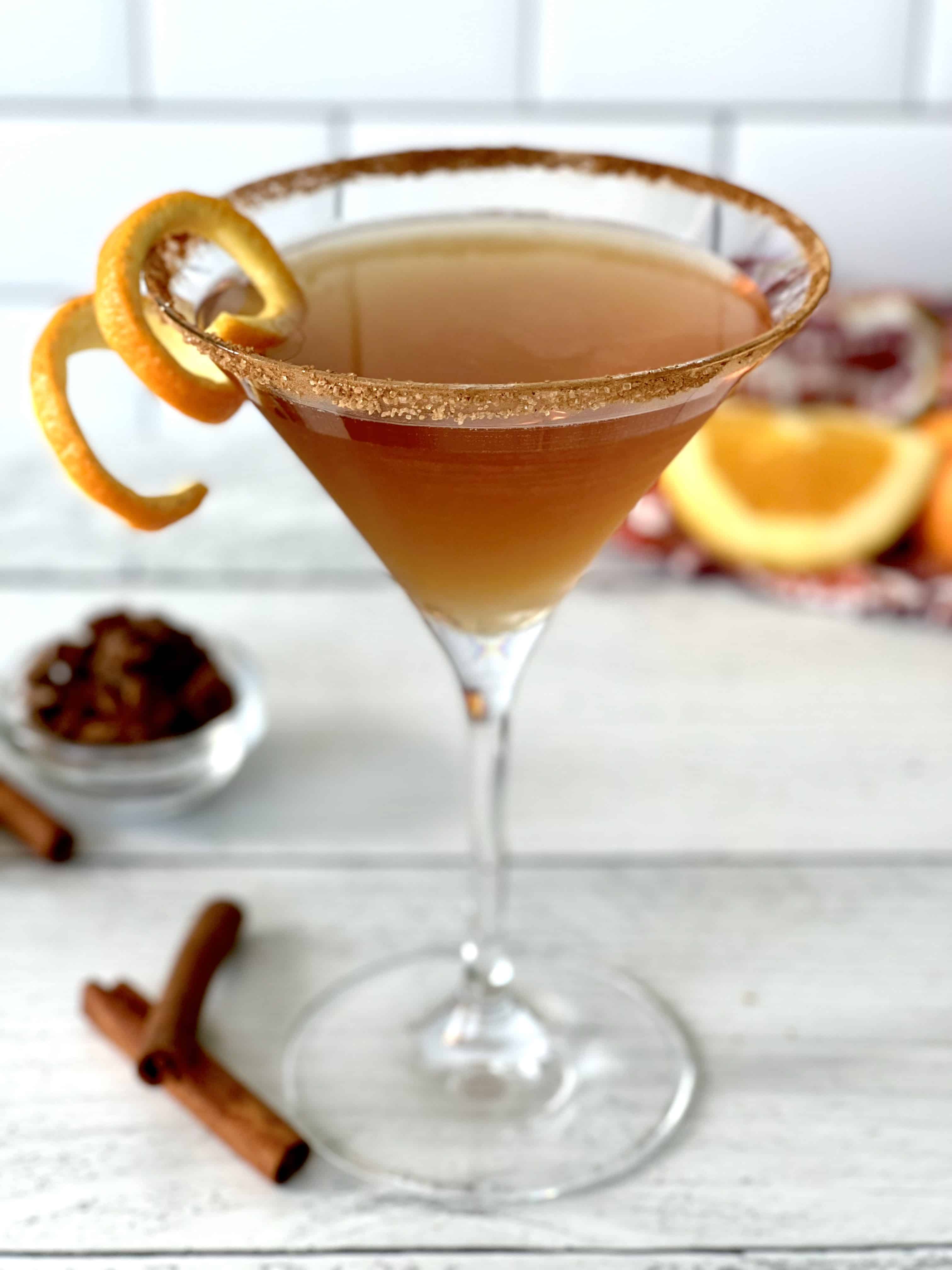 A chai vodka martini in a martini glass with a cinnamon sugar rim and an orange peel twist on the rim
