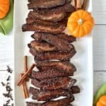 bacon candy on a white rectangular platter with mini pumpkins, cinnamon sticks and whole cloves