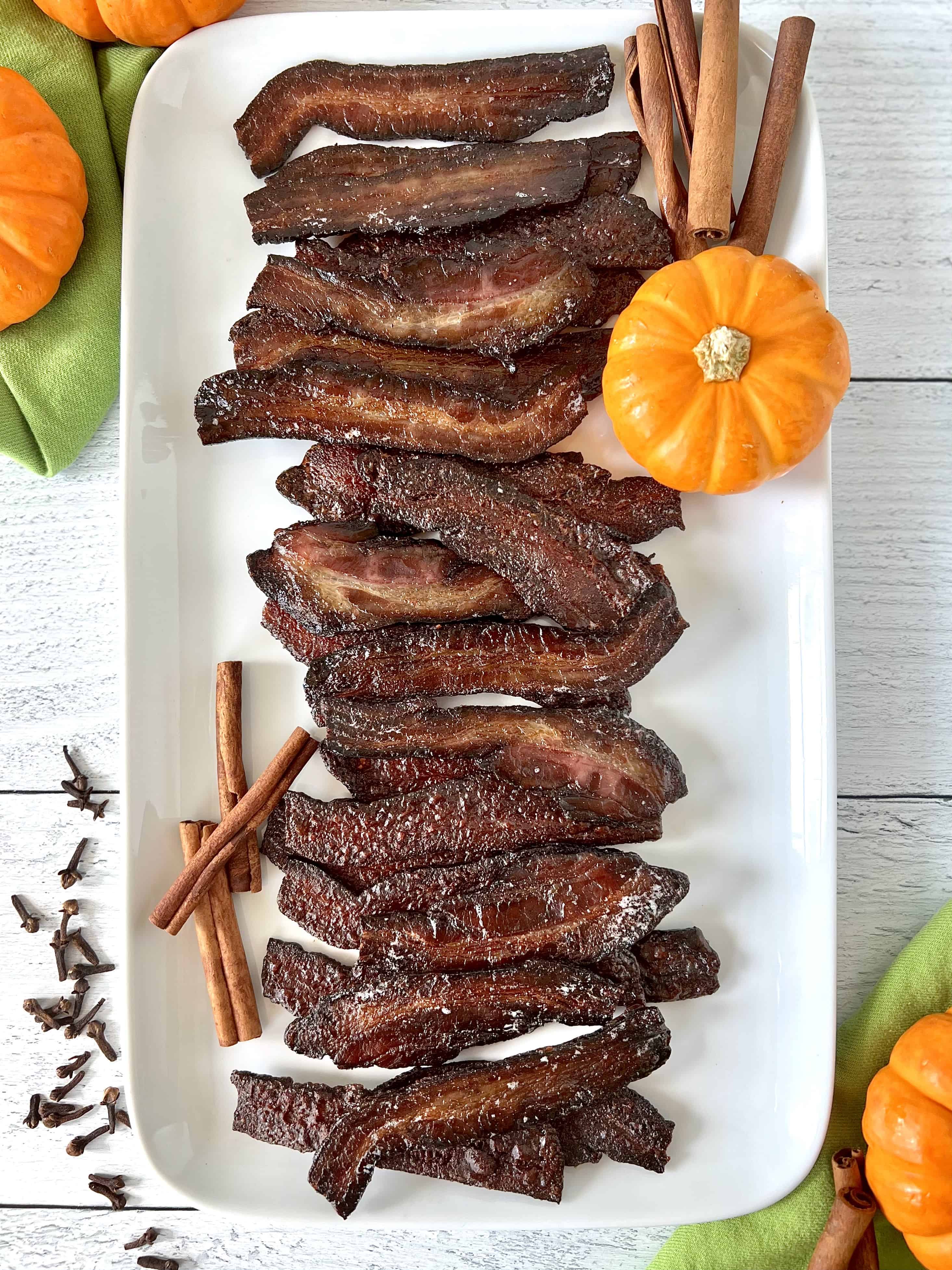 bacon candy on a white rectangular platter with mini pumpkins, cinnamon sticks and whole cloves
