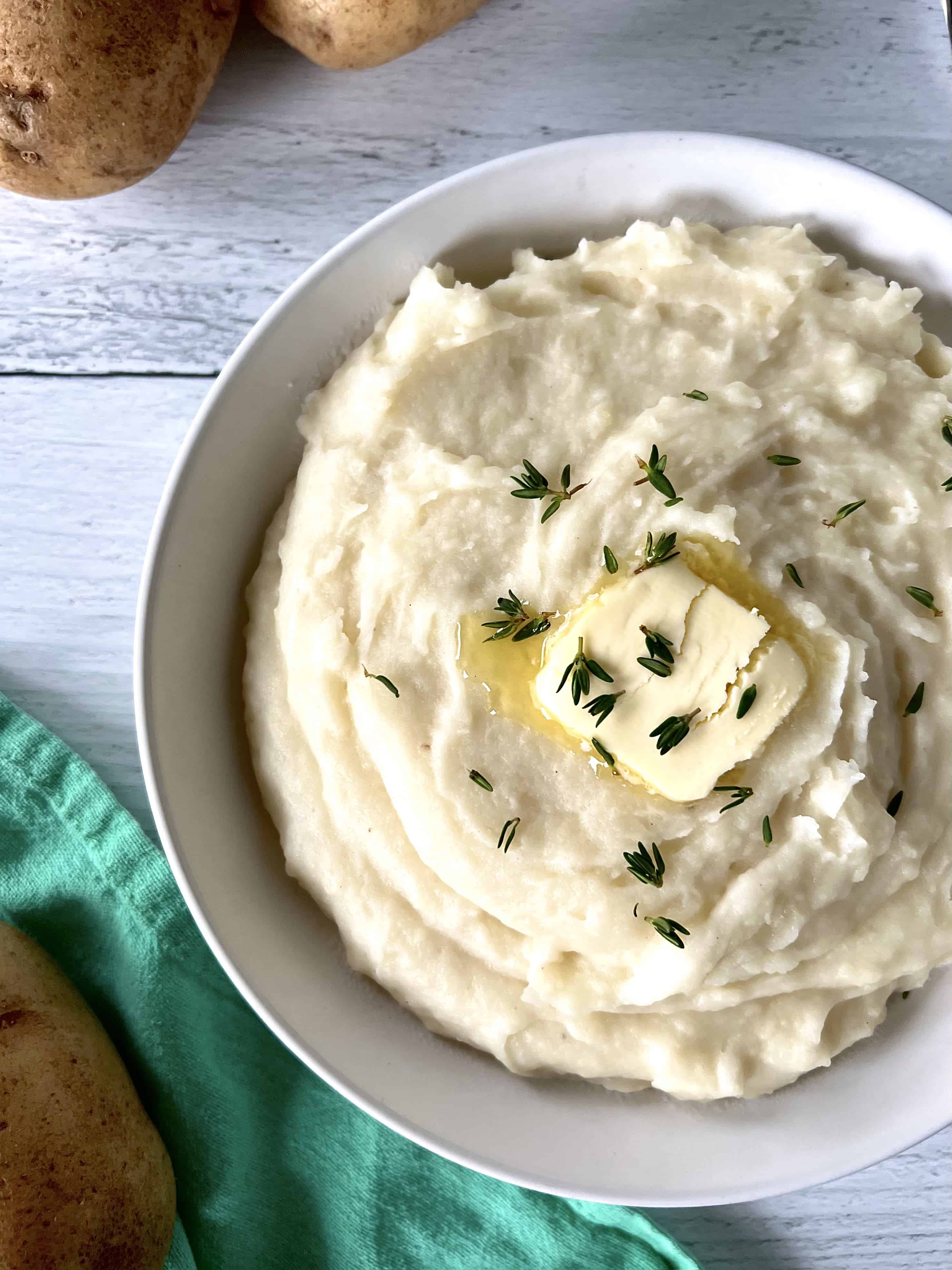 healthy homemade mashed potatoes in a white bowl topped with a pat of ghee and fresh thyme