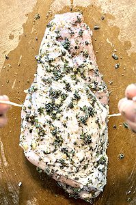 a turkey breast coated in herbs with 2 hands about to tie it up with twine