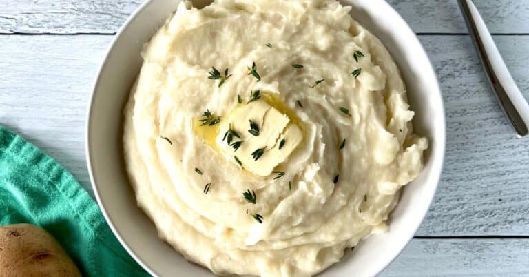 dairy-free mashed potatoes in a white bowl topped with a pat of melting ghee and fresh thyme