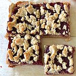 vegan cranberry bars on parchment paper with a bowl of cranberry sauce