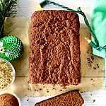 grain free gingerbread sliced on parchment paper on a white wooden table between Christmas lights, a green napkin, a green ornament and small bowls of spices