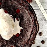 Chocolate Paleo skillet cake in a cast iron skillet topped with a scoop of vanilla ice cream, next to chocolate chips and an ice cream scoop.