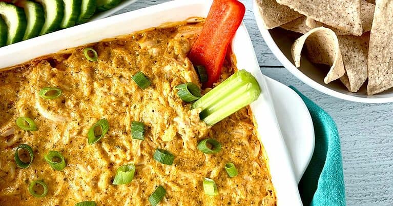Whole30 buffalo chicken dip in a white square baking dish with a celery stalk and red pepper slice sticking out of the corner