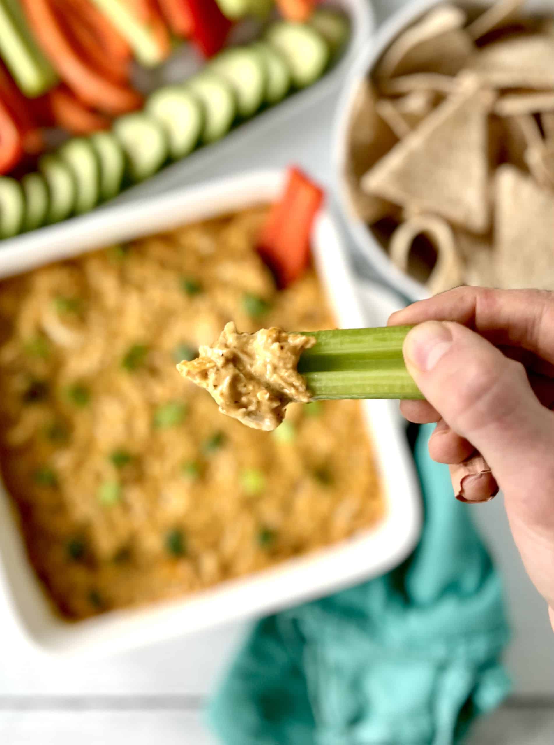 a hand holding a celery stick with healthy Whole30 dip made with shredded chicken, mayo and dairy-free cream cheese