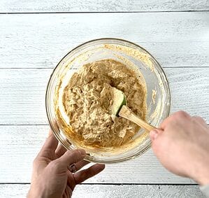 A hand holding a green spatula as it stirs Paleo buffalo chicken dip in a glass bowl.