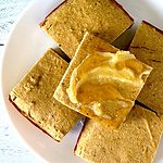Corn-free cornbread squares piled on a plate with the top one covered in ghee and honey.
